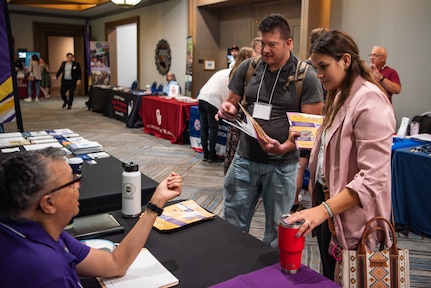 Attendees talk to a woman at a booth