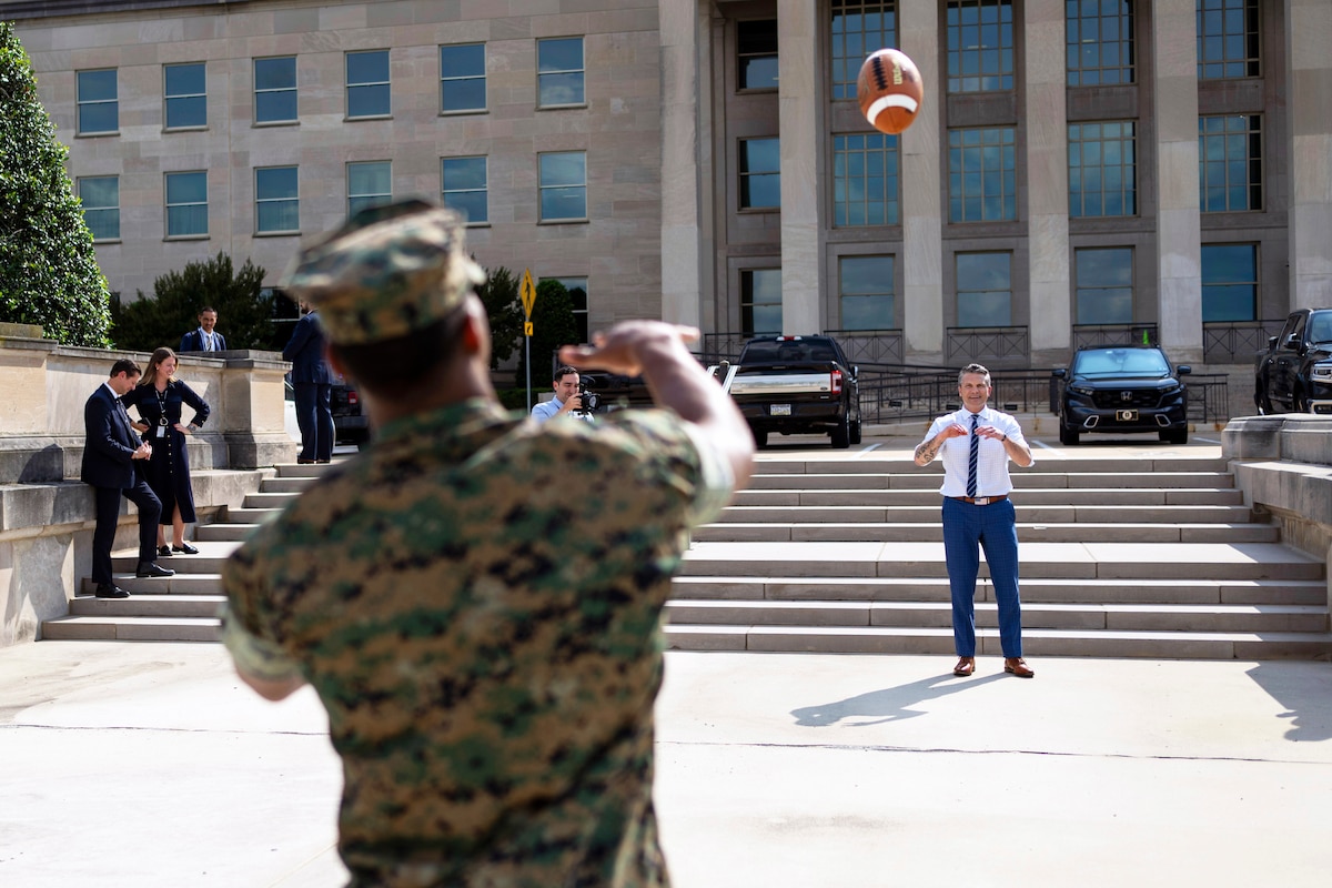A Marine in uniform tosses a football to Defense Secretary Pete Hegseth outside the Pentagon.