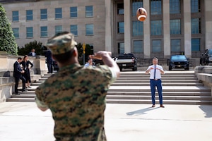 A Marine in uniform tosses a football to Defense Secretary Pete Hegseth outside the Pentagon.