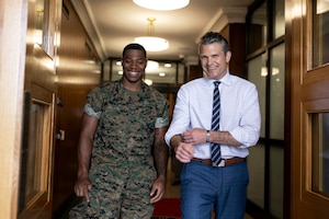 Defense Secretary Pete Hegseth and a Marine stand and smile next to each other in a hallway.