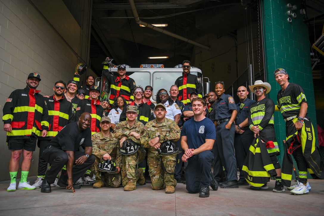 Service members and firefighters pose with a baseball team and a firetruck.