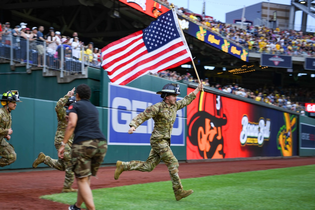 Service member carries a flag on a baseball field.