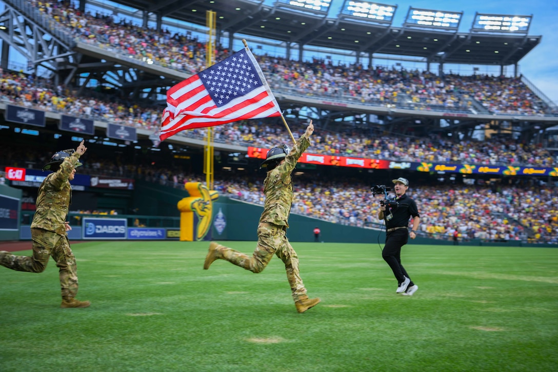 Service member carries a flag on a baseball field.
