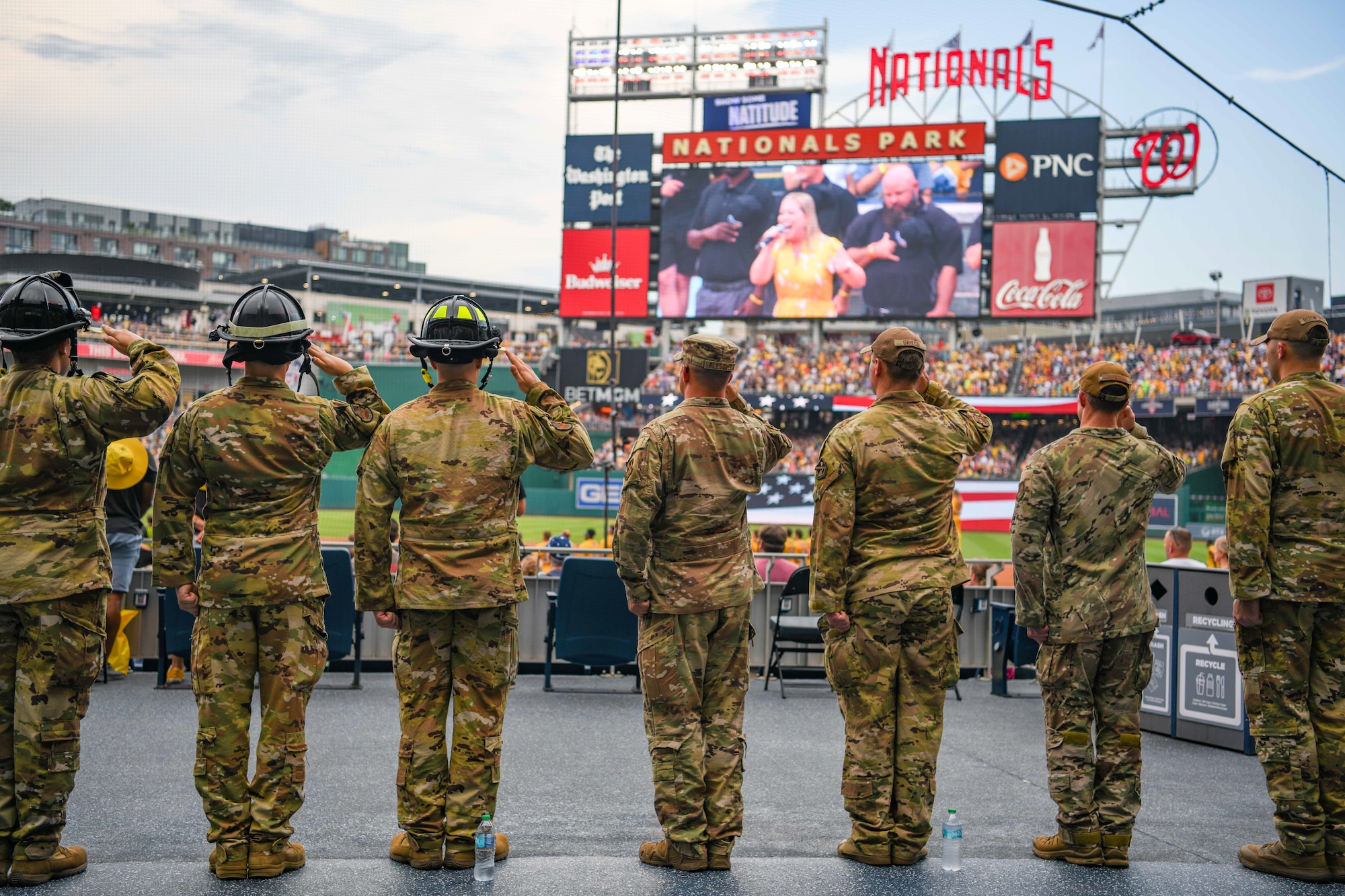 Service members salute during a baseball game.