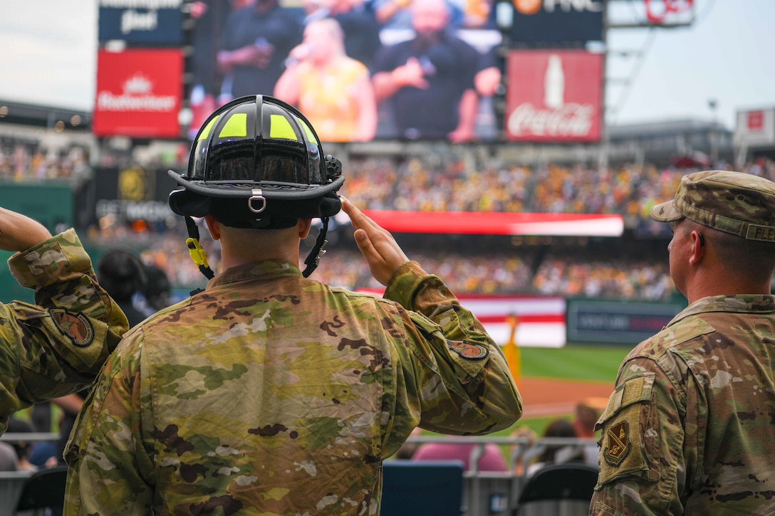Firefighter salutes during a baseball game.