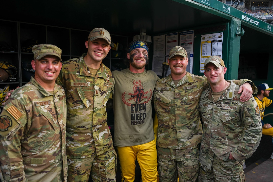 Service members take a picture with a baseball player in the dugout.