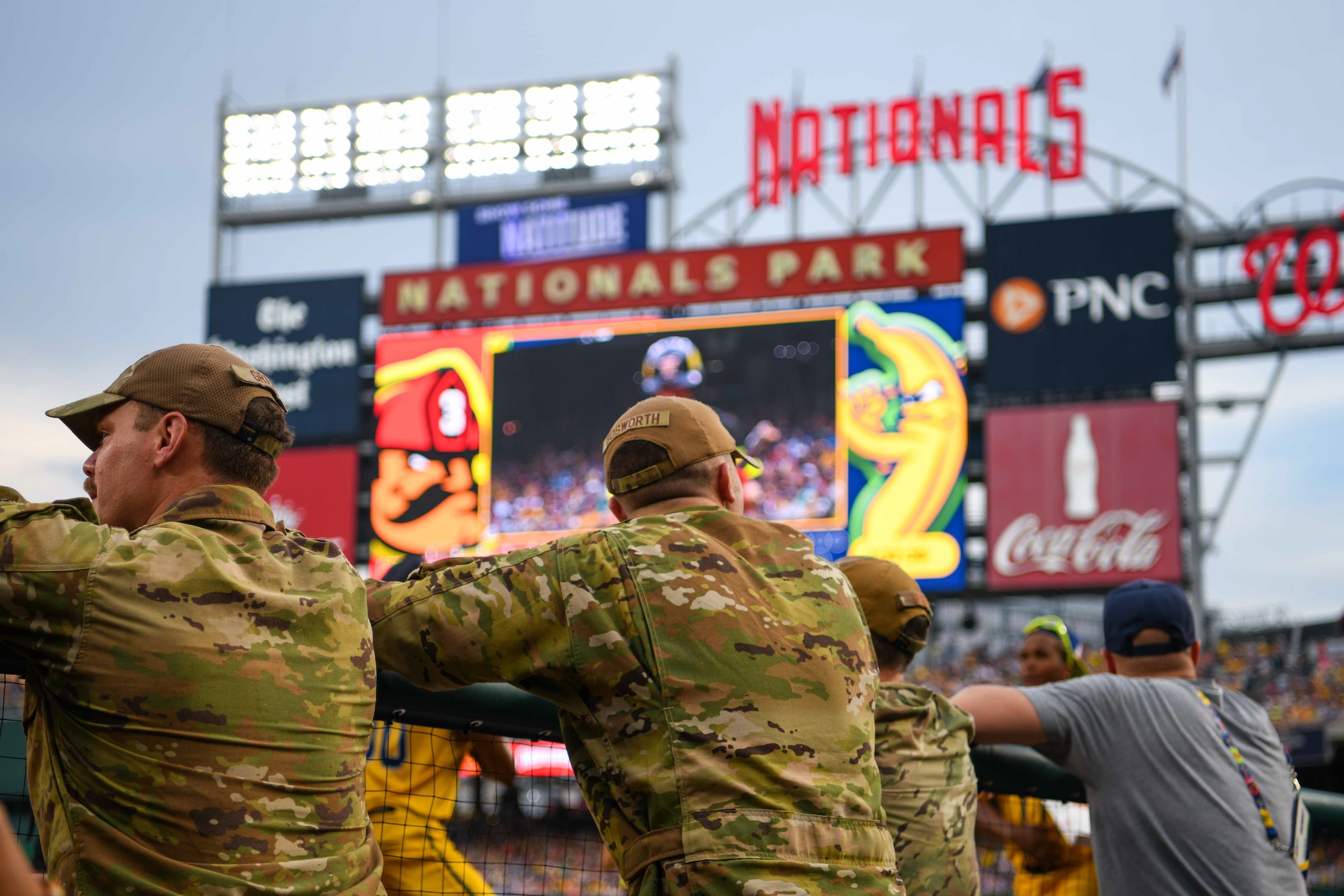 Service members watch a baseball game from the dugout.
