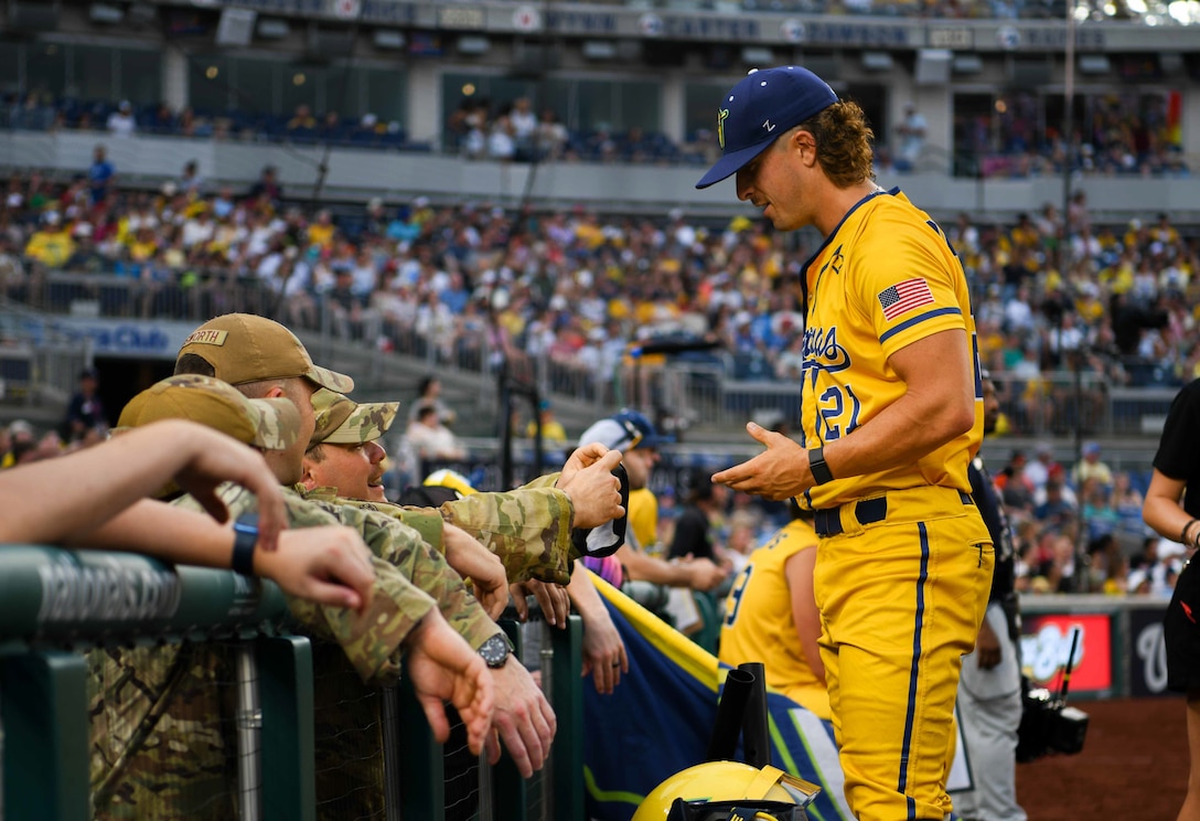 A baseball player talks to service members in the dugout.