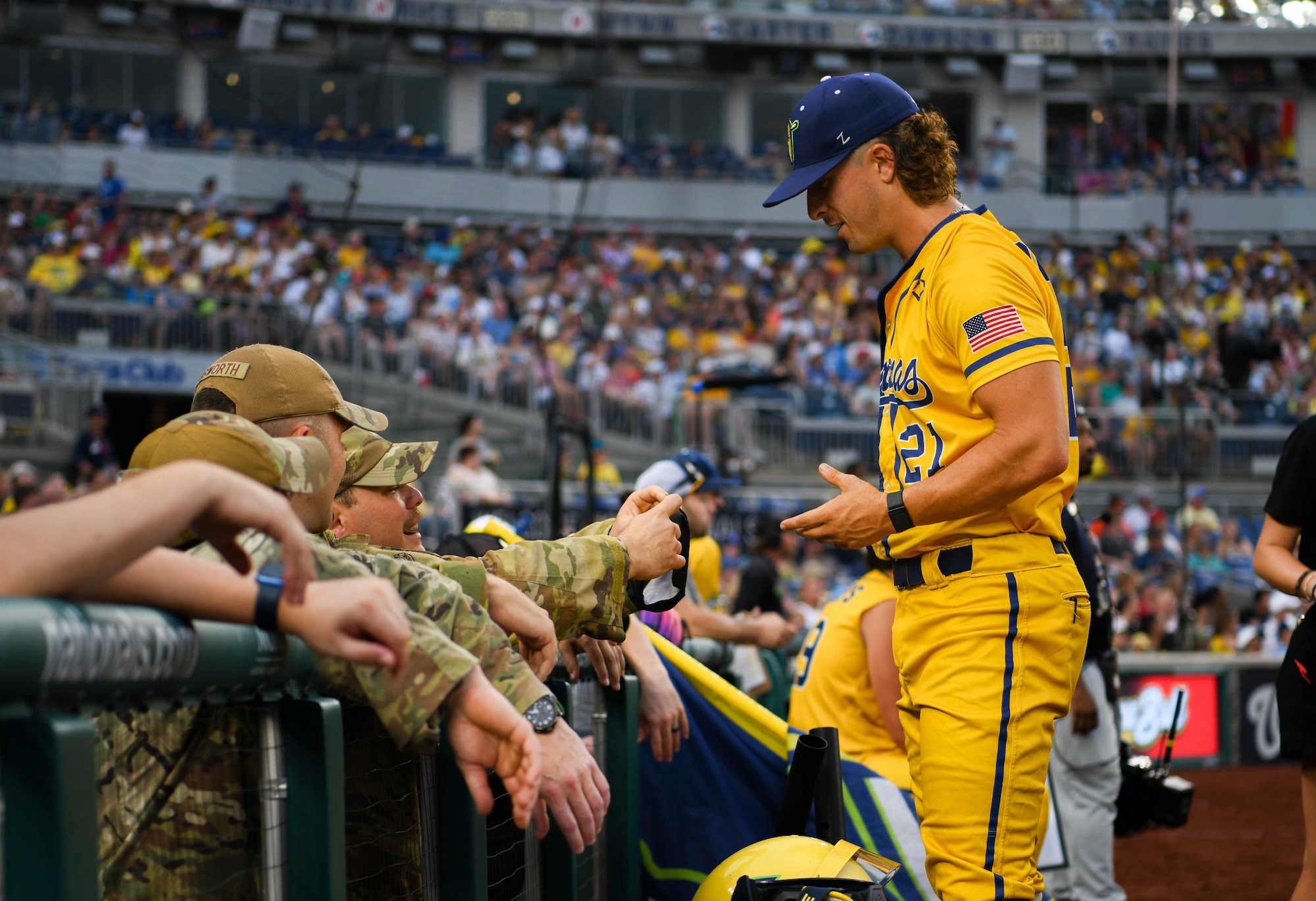 A baseball player talks to service members in the dugout.