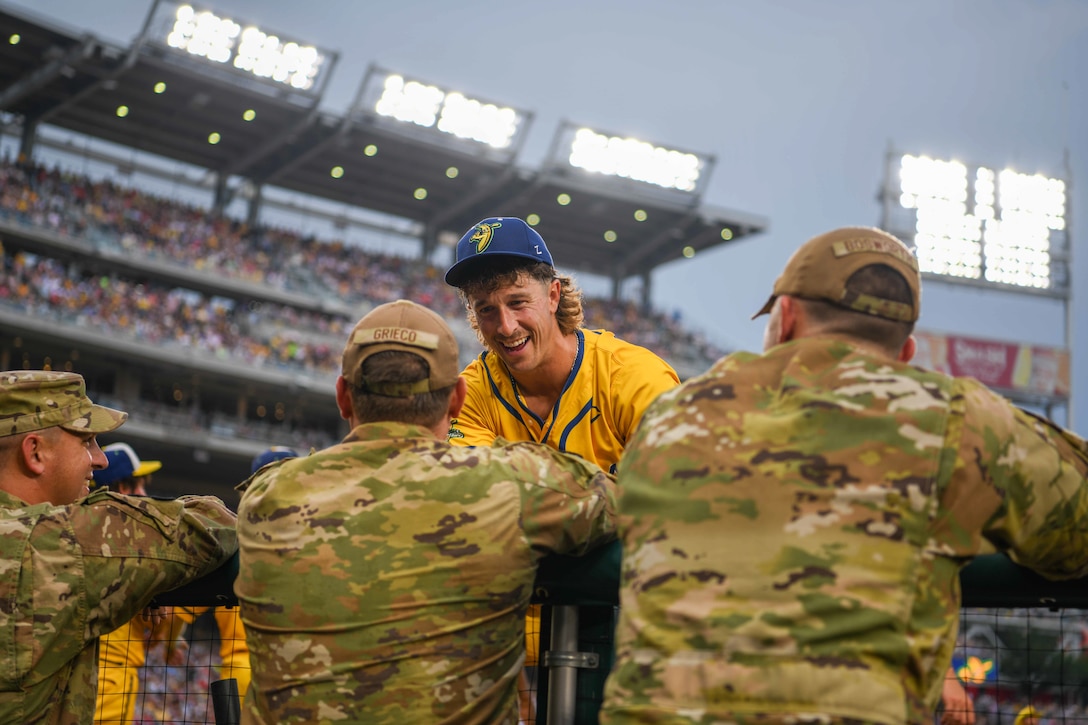 A baseball player talks to service member in the dugout.