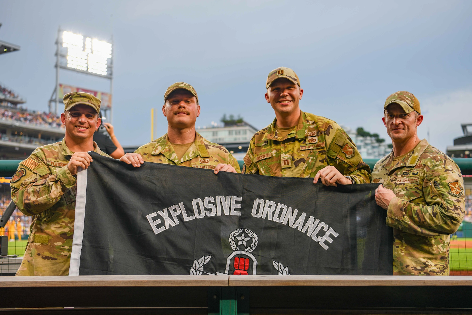 Service members hold up a flag in the dugout of a baseball stadium.