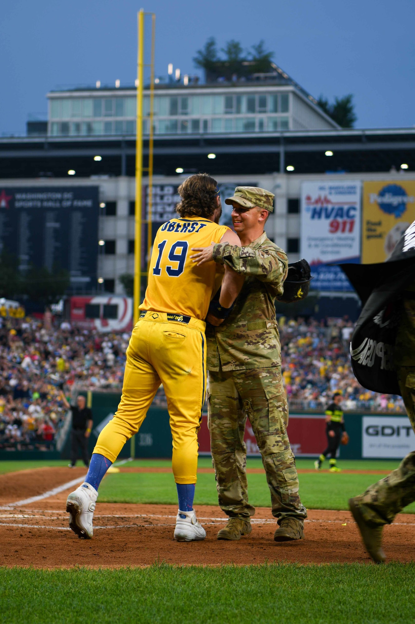 Service member hugs a baseball player.