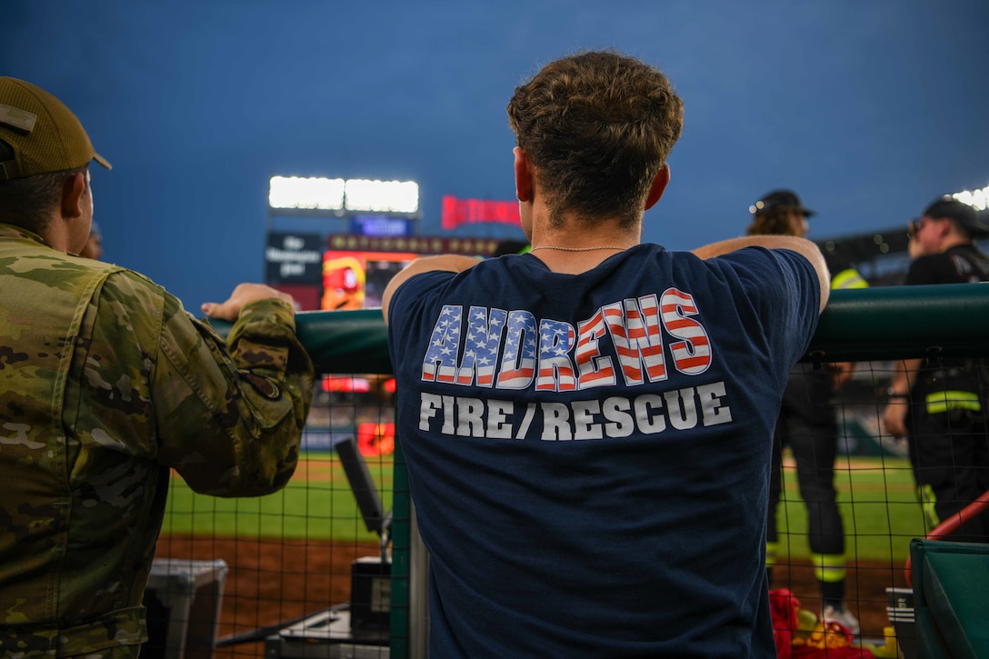 A firefighter watches a baseball game from the dugout.