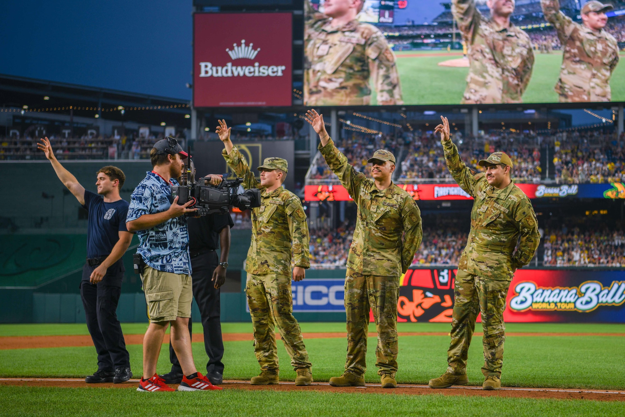 Service members wave on a baseball field.