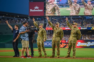 Service members wave on a baseball field.