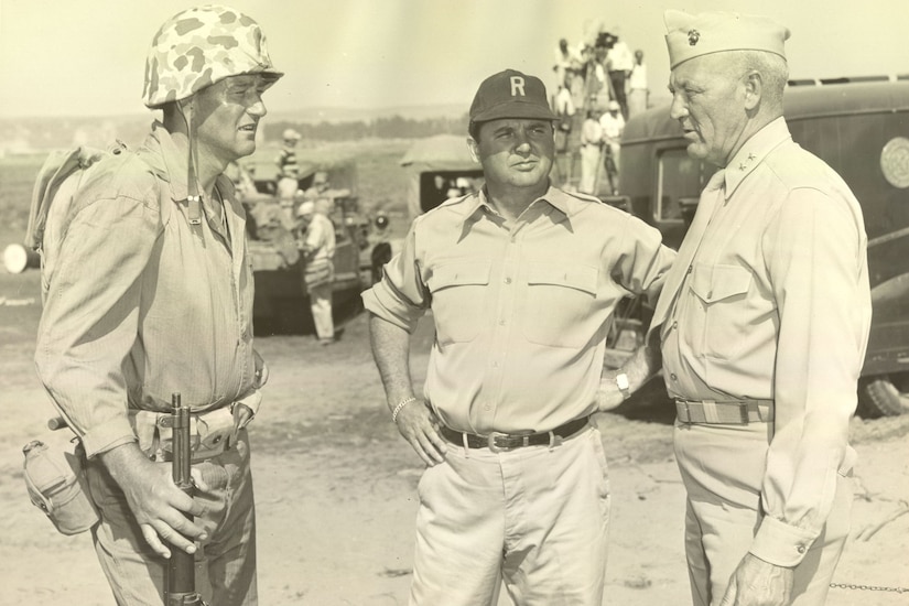 A man dressed in a Marine Corps uniform speaks to two other men wearing military uniforms.