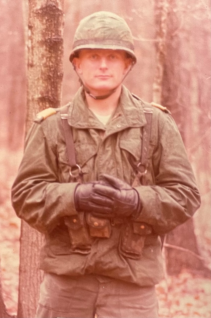 A man dressed in a winter military uniform stands in a forest.