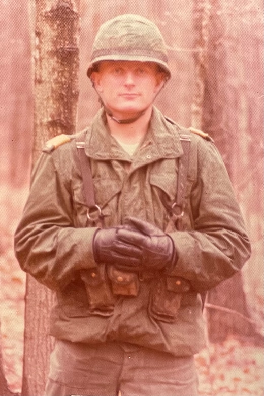 A man dressed in a winter military uniform stands in a forest.