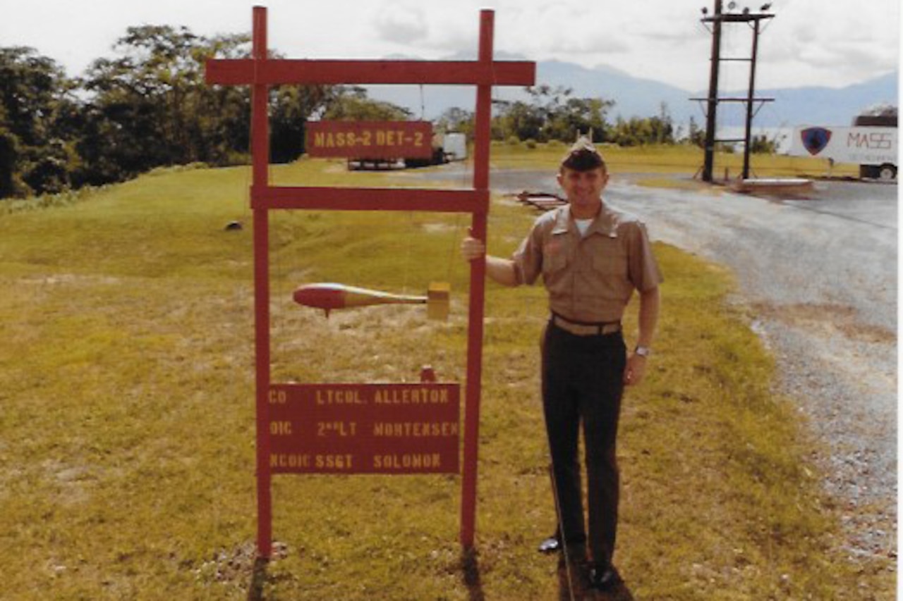 A man dressed in a military uniform stands beside a sign.