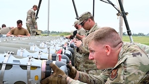 Airmen guide a munition down a conveyer belt.