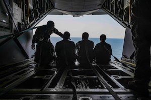 A U.S. Air Force loadmaster assigned to the 1st Special Operations Wing and Air Force Junior ROTC cadets look out the back of a 1st SOW MC-130J Commando II during an orientation flight near Hurlburt Field, Florida, June 25, 2025.