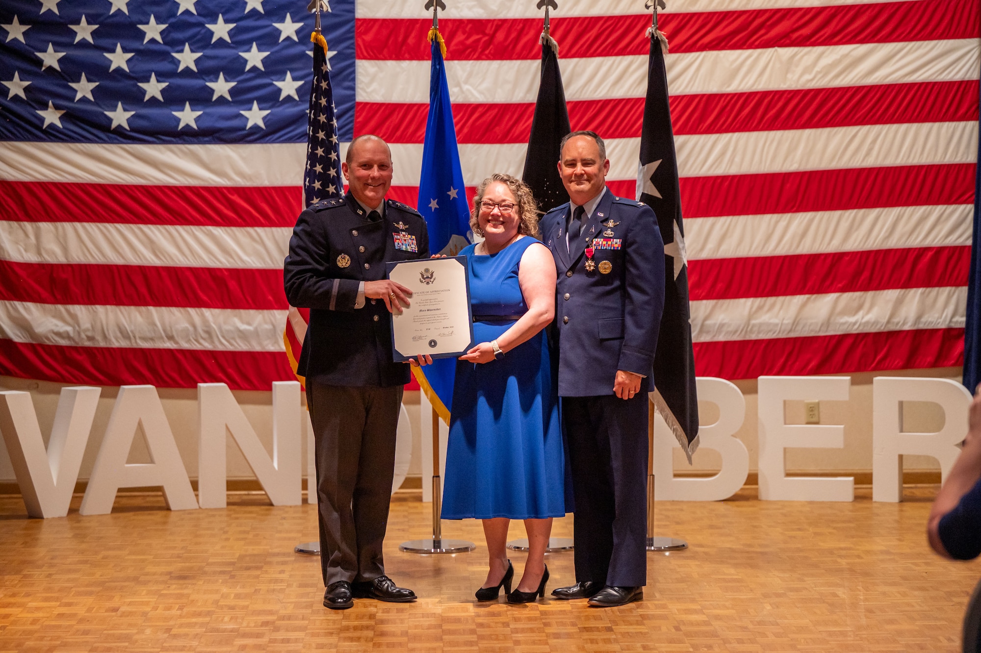 Three people pose on a stage inside.
