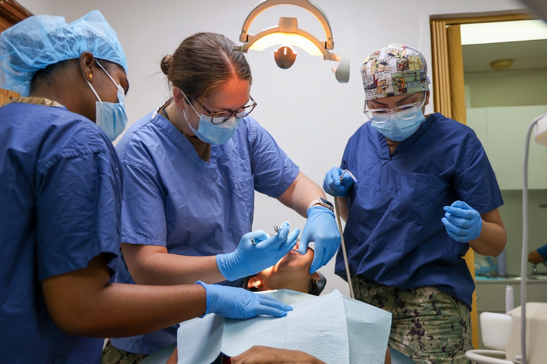 Dental personnel in scrubs work on a patient under a spotlight.