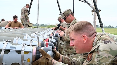 Airmen guide a munition down a conveyer belt.