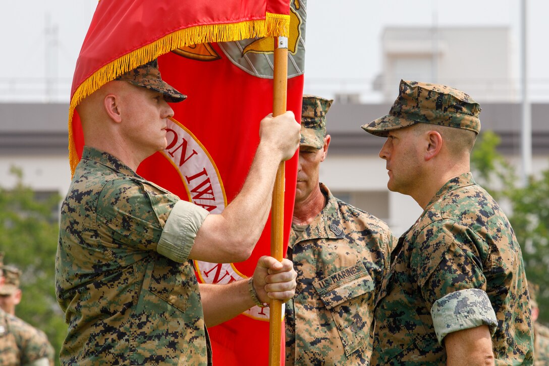 U.S. Marine Corps Col. Kenneth Rossman, left, oncoming commanding officer, Marine Corps Air Station Iwakuni, takes the station colors from Col. Richard Rusnok, right, outgoing commanding officer, MCAS Iwakuni, during a change of command ceremony at MCAS Iwakuni, Japan, July 2, 2025. MCAS Iwakuni held the change of command ceremony to formally transfer command from Col. Richard Rusnok to Col. Kenneth Rossman, symbolizing the shift in leadership, authority, and responsibility for the installation. (U.S. Marine Corps photo by Lance Cpl. David Getz)