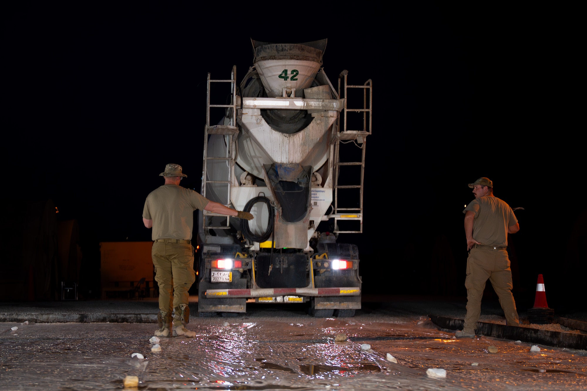 Two U.S. Air Force Airmen direct a cement truck to a job site at night.