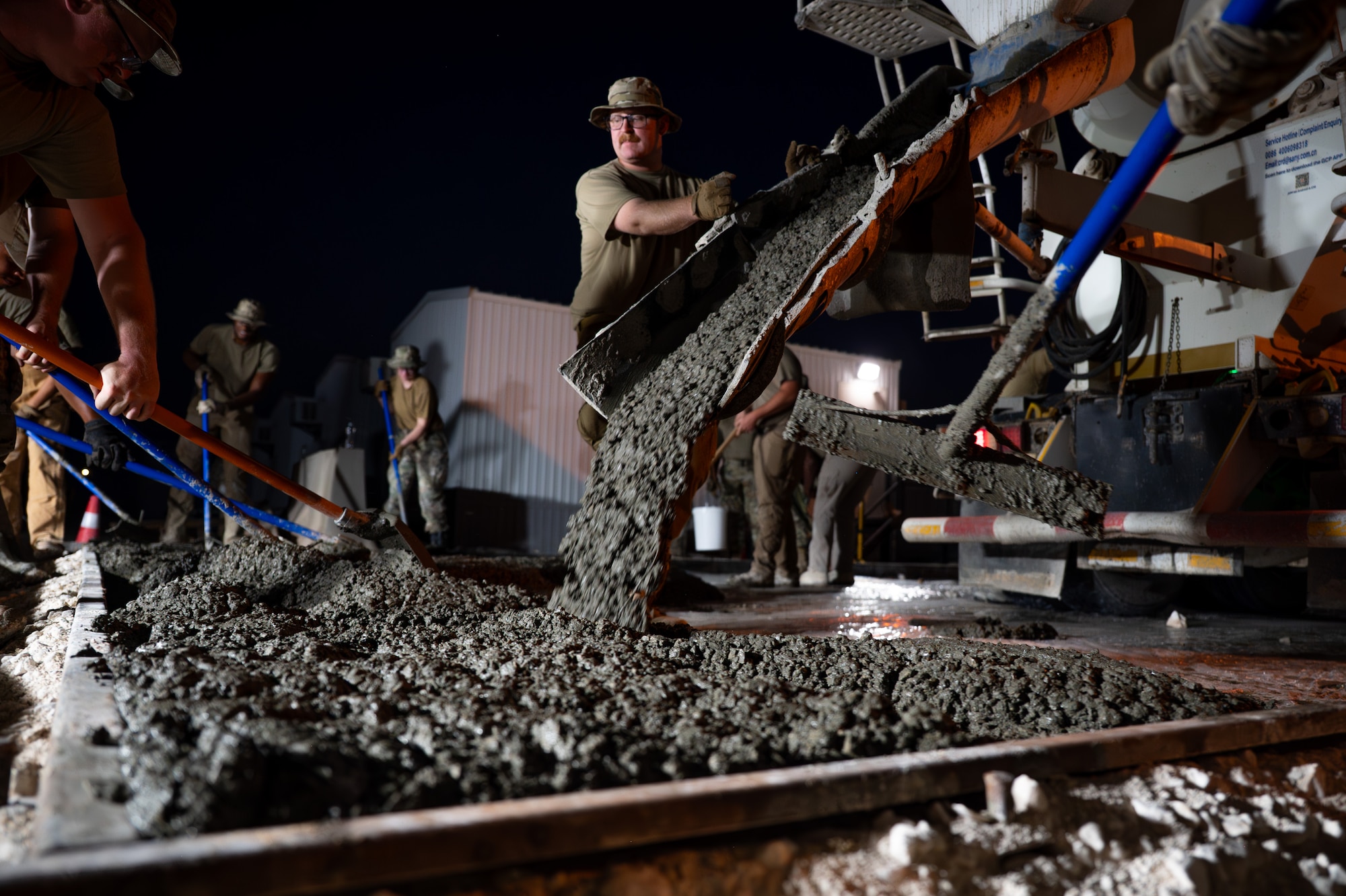 U.S. Air Force Airman holds a concrete truck chute as wet concrete pours into a mold.