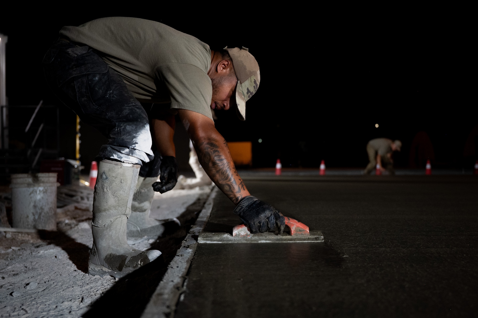 U.S. Air Force Airman uses a tool to level a wet concrete pad at night.