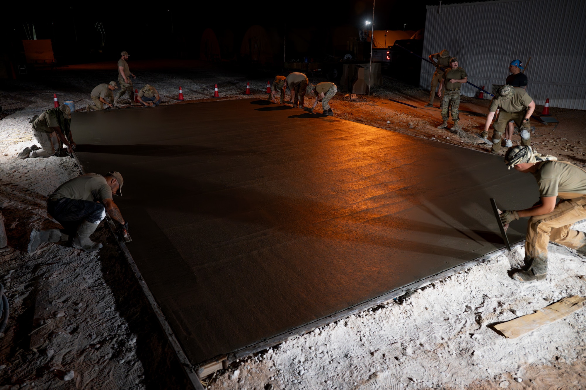 A group of U.S. Air Force Airmen work on a wet concrete pad at night