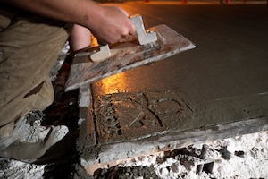 U.S. Air Force Airman pulls a concrete stamp with "DIRTBOYZ" from a wet concrete pad at night