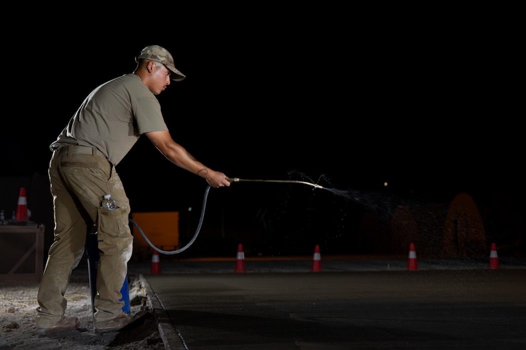 U.S. Air Force Airman sprays curing compound on a newly laid concrete pad at night