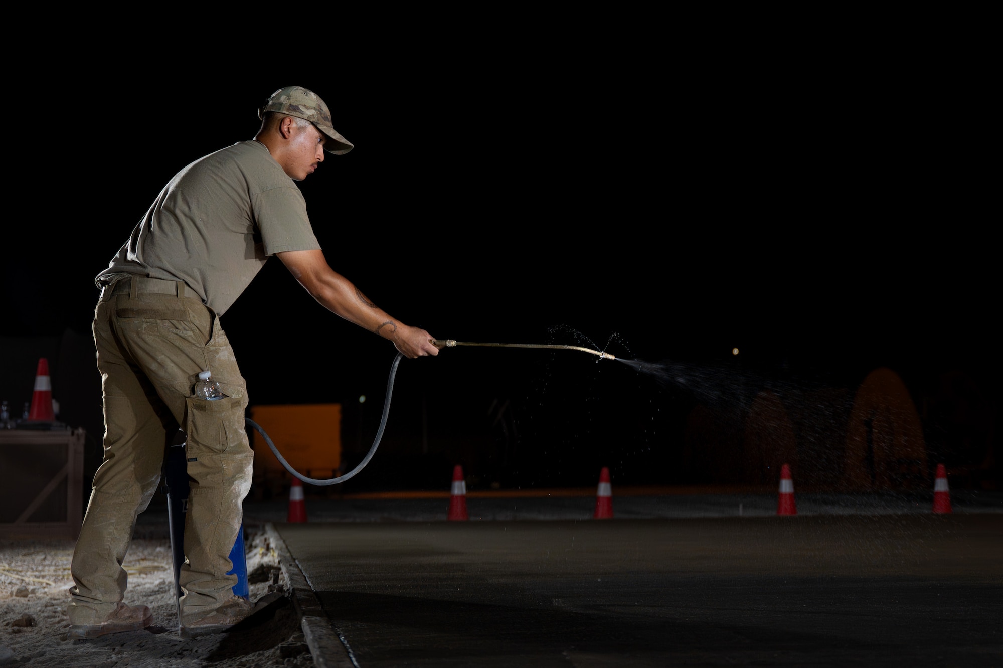 U.S. Air Force Airman sprays curing compound on a newly laid concrete pad at night