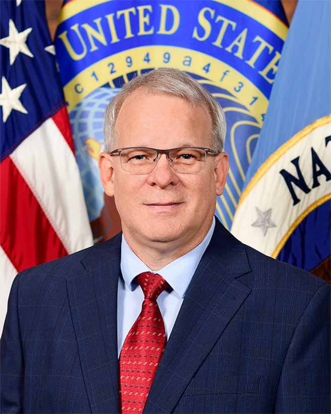 Portrait of a man in a suit, standing in front of multiple flags