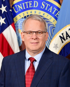 Portrait of a man in a suit, standing in front of multiple flags