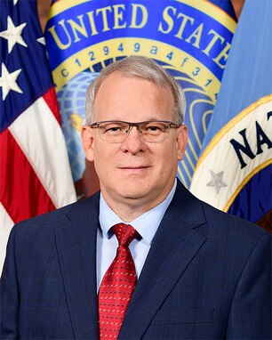 Portrait of a man in a suit, standing in front of multiple flags
