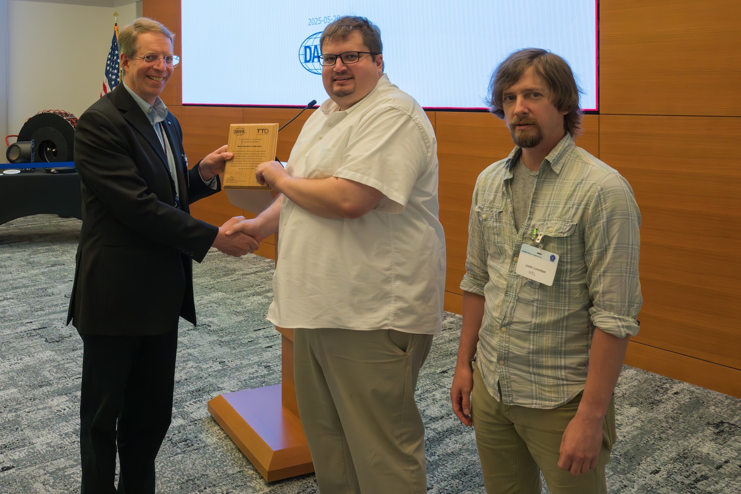 Three gentlemen stand together holding an award
