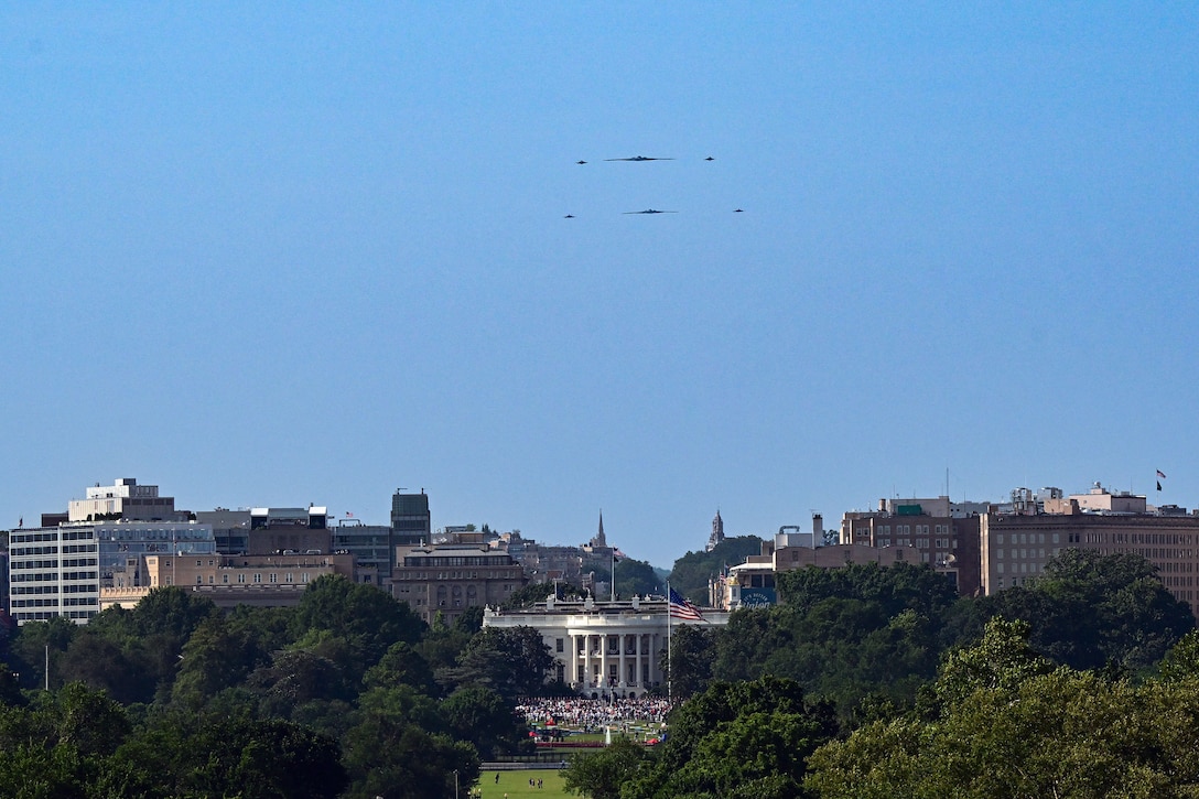 Six aircraft fly in formation in a blue sky over the White House as hundreds gather on the lawn.