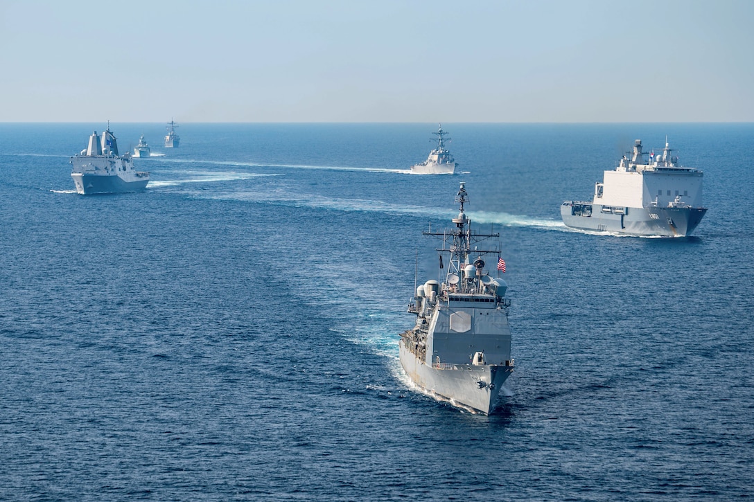 U.S., Canadian and Dutch ships sail in formation in blue waters during the day.
