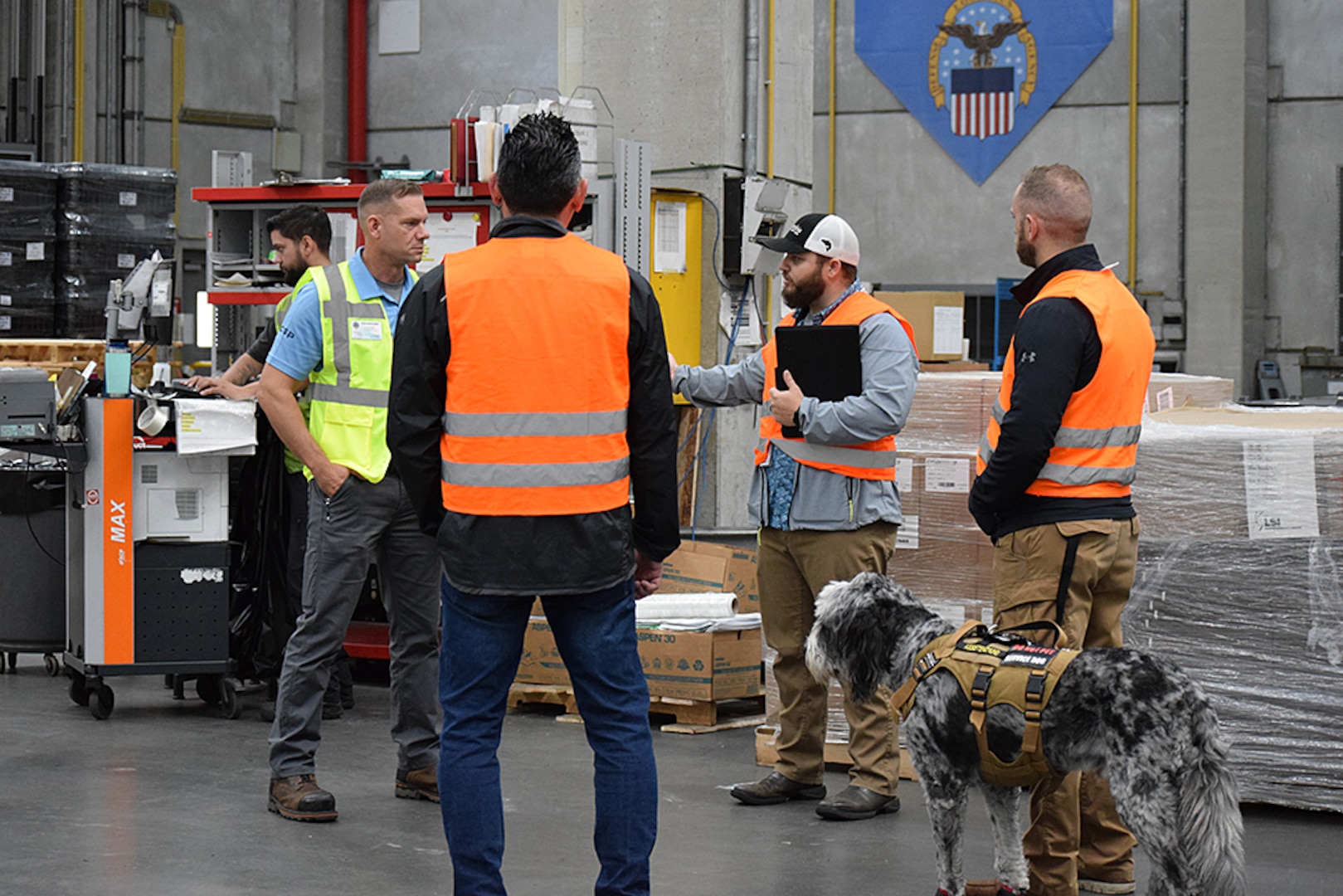 Men and a dog talk in a warehouse.