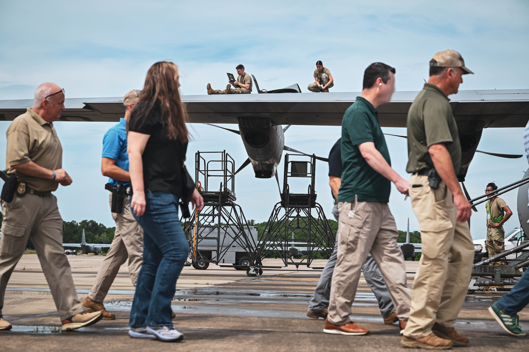 Men and women walk past a team of aircraft maintainers working on the wing of an aircraft.
