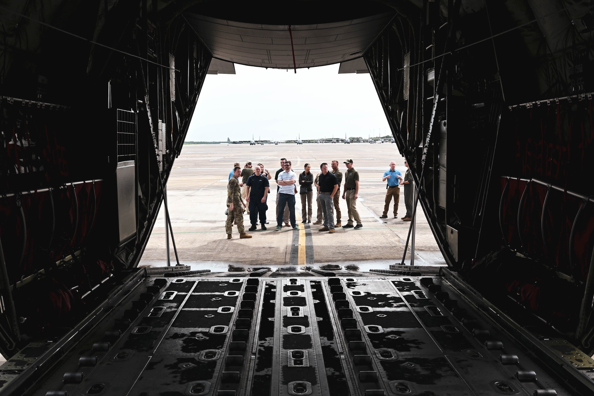 Men and women stand beside the cargo ramp and door of an aircraft.