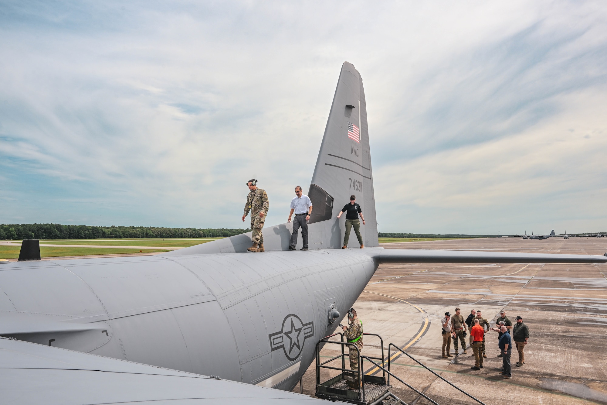 A man in uniform escorts two civilians on the top of an aircraft.