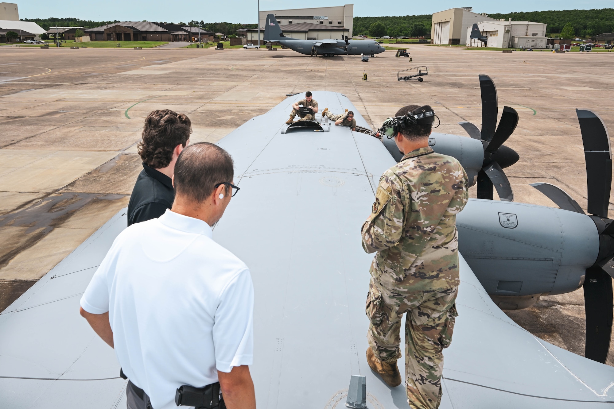 A man in uniform shows two civilians what maintainers are doing on a plane.