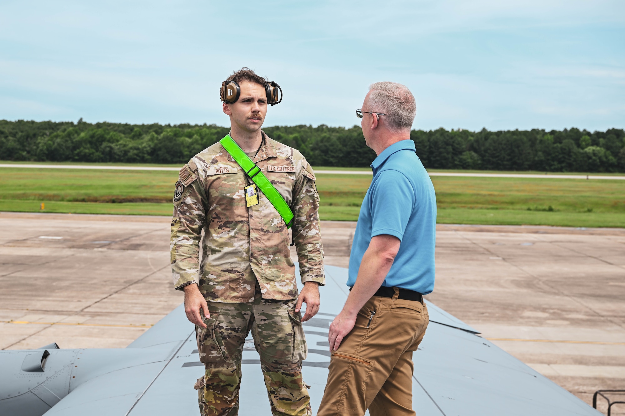 A man in uniform speaks to a civilian on top of an aircraft.
