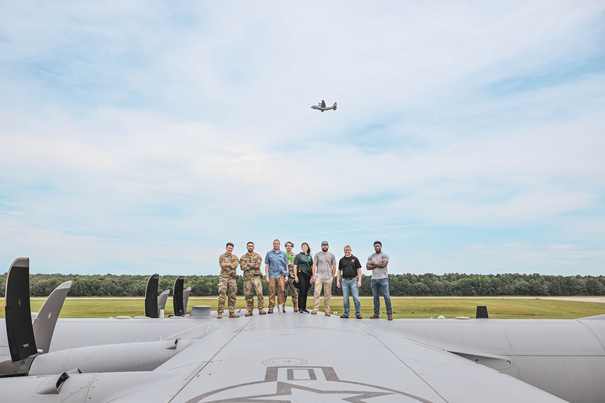 Military members and civilians pose for a photo on top of an aircraft.
