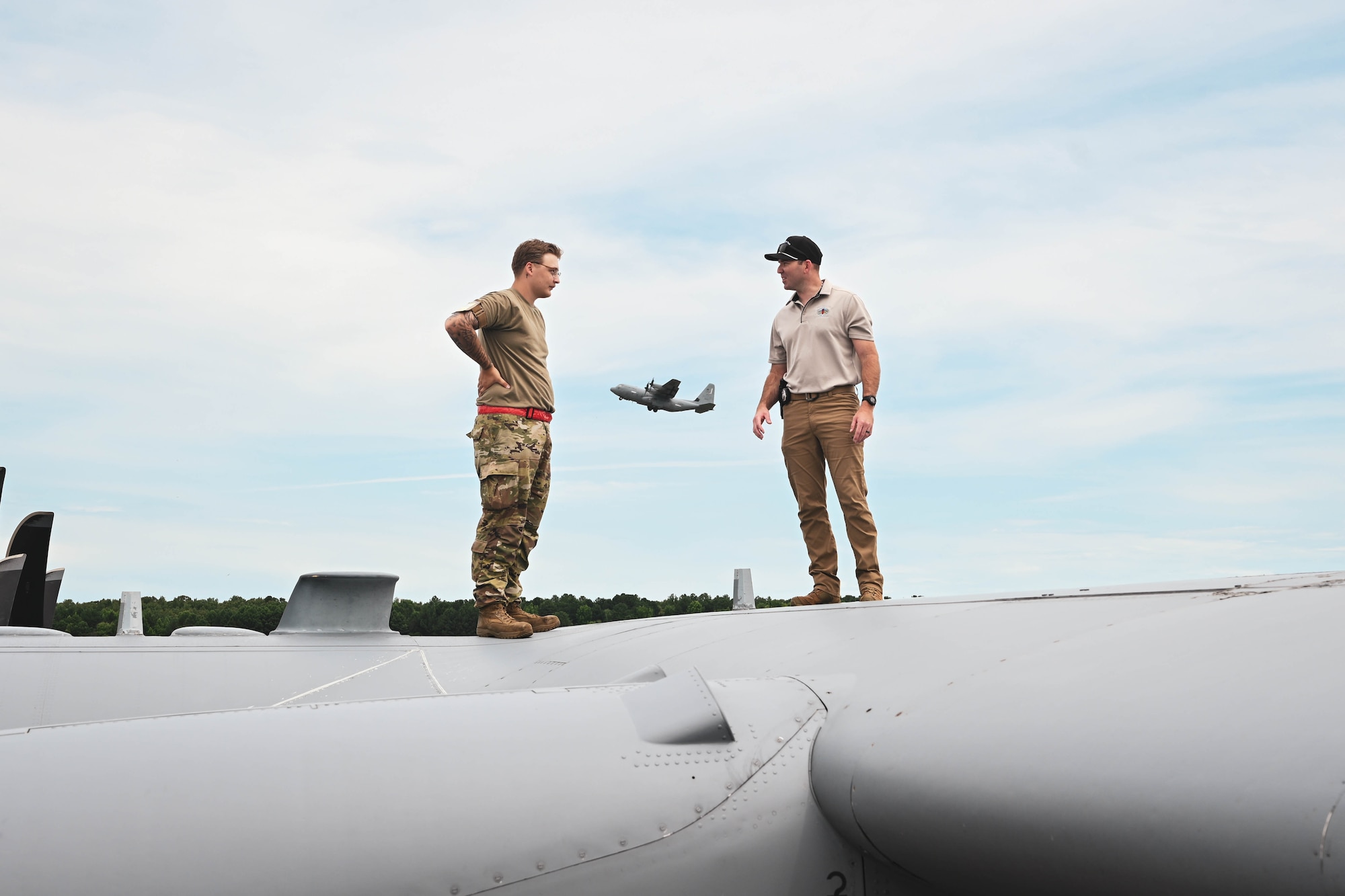 A man in uniform stands with a civilian on top of an aircraft.
